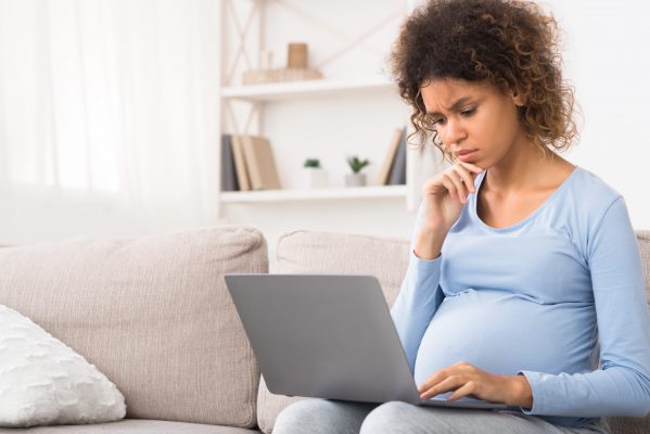 Confused afro expectant woman using laptop, buying goods for newborn baby, free space